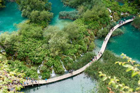 Plitvice Lakes National Park - UNESCO World Heritage Centre. Aerial view, colorful spring panorama of lit by sun green forest and long wooden bridge with tourists over blue lake with blue-green water.の写真素材