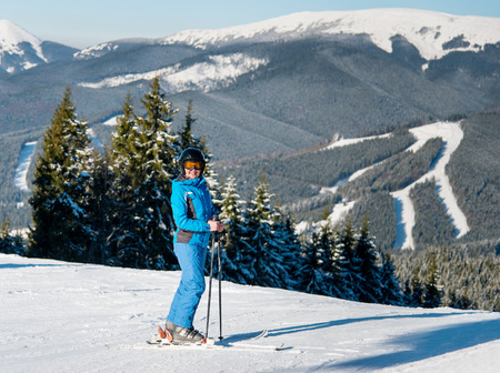 Full length shot of a happy woman skier skiing on the slope at winter ski resort in sunny beautiful day. Mountains, forests, ski slopes on the background. happiness activity recreation sports conceptの写真素材