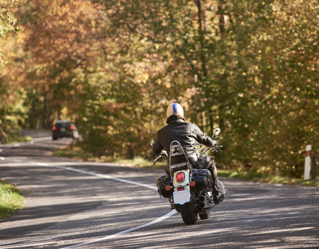 Back view of motorcyclist in black leather jacket and helmet riding motorbike along twisted asphalt...