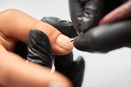 Process of making fashionable manicure in beauty salon. Close-up of professional master manicurist hands painting patterns on client woman nails using applicator on light blurred background.の写真素材
