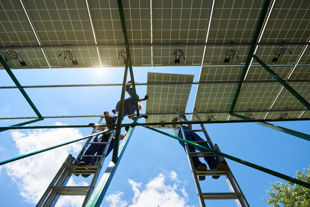 Installing innovative solar batteries by workers. standing on high ladder. Sunny weather, blue sky. Modern solution for natural resources saving, using renewable solar energy. environment friendly.の写真素材