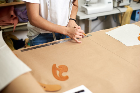 Working place in design studio, pattern creation process. Female designer hands close-up making drawing lines on cardboard using pencil and ruler. Exclusive clothes making, creative occupation conceptの写真素材