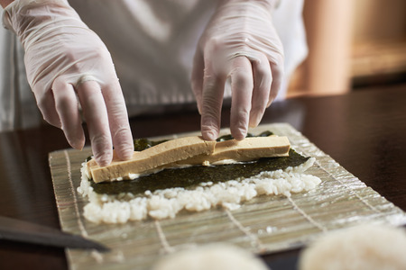 Close-up view of process of preparing rolling sushi with nori, rice and omelet on bamboo matの写真素材