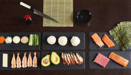 Preparing rolling sushi. Ingredients on the black stone plates with knife, bamboo mat and bowl. View from the topの写真素材