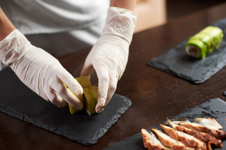 Closeup view of process of preparing rolling sushi. Master is serving fresh delicious rolls on the black stone plateの写真素材