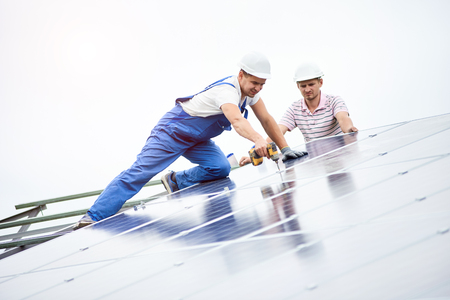 Construction worker connects photo voltaic panel to solar system using screwdriver. Professional installing and construction of solar system, alternative energy and financial investment concept.の写真素材