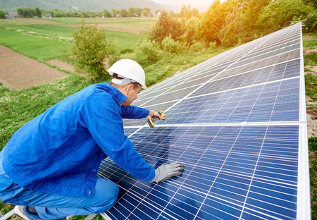 Construction worker connects photo voltaic panel to solar system using screwdriver. Professional installing and construction of solar system, alternative energy and financial investment concept.の写真素材