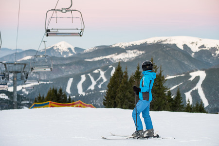 Woman skier on slope in the mountains of winter resort. Woman at ski resort wearing helmet, blue ski suit and gogglesの写真素材