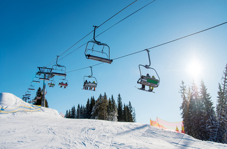 Low angle shot of a ski lift at ski resort Bukovel in the mountains on a sunny winter day. Blue sky, sun and forest on the background copyspace riding top nature extreme sport recreation conceptの写真素材