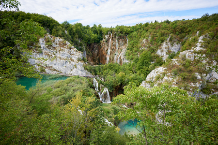 Plitvice Lakes National Park Aerial view, colorful spring panorama of lit by sun green forest and long wooden bridge with tourists over blue lake with blue-green water.の写真素材