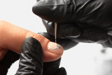 Close-up of professional manicurist hands painting elegant abstract silver glitter pattern on client woman painted nails using thin applicator brush in beauty salon on bright white background.の写真素材