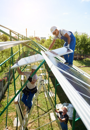 Professional workers team installing solar panels on the green metal construction using different equipment. Innovative solution for energy solving. Use renewable resources. Green energy.の写真素材