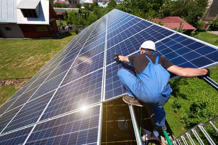 Professional worker installing solar panels on the green metal construction, using different equipment, wearing helmet. Innovative solution for energy solving. Use renewable resources. Green energy.の写真素材