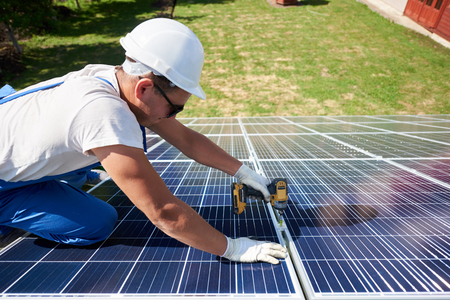 Professional worker installing solar panels on the green metal construction, using different equipment, wearing helmet. Innovative solution for energy solving. Use renewable resources. Green energy.の写真素材