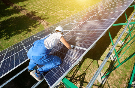 Professional worker installing solar panels on the green metal construction, using different...