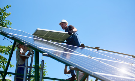 Professional workers team installing solar panels on the green metal construction using different equipment. Innovative solution for energy solving. Use renewable resources. Green energy.の写真素材