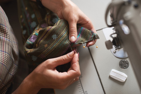 Tailor workplace: electrical sewing machine blurred background and close-up of female hands pinning...