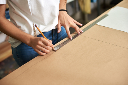 Working place in design studio. Professional female designer hands close-up making paper patterns using measuring tape, ruler. Exclusive clothes making, creative occupation concept.の写真素材