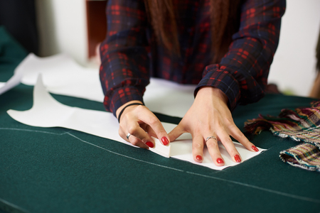 Tailor, designer workplace in atelier. Female hands making white chalk markings of paper patterns on green fabric copy space surface before cutting details for future jacket or costume.の写真素材