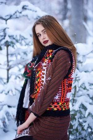 Portrait of attractive young slim girl with long straight loose hair in long woolen stylish dress and dark kerchief with bright floral pattern outdoors i on sunny snowy winter day.の写真素材