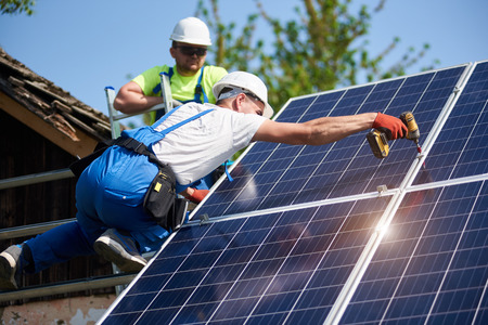 Two workers technicians connecting heavy solar photo voltaic panels to high steel platform. Exterior solar system installation, alternative renewable green energy generation concept.の写真素材