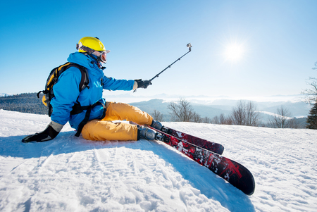 Shot of a skier sitting on the ski slope taking a selfie using selfie stick resting relaxing extreme recreation active lifestyle activity technology smart phone mobility internet online concept.の写真素材