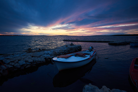 Beautiful summer seascape at sunset. Small boats anchored in sea inlet calm shallow water lit by red sun rays of setting sun. Tourism, fishing, diving, recreation and beauty of nature concept.の写真素材