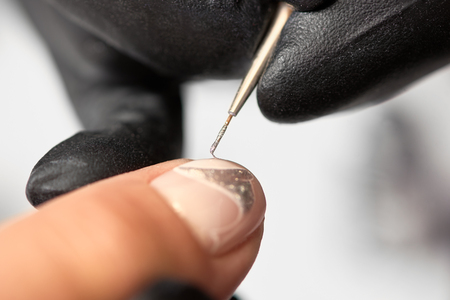 Fashionable manicure in beauty salon. Close-up of professional manicurist hands in black rubber gloves painting elegant abstract silver patterns on client woman nails using thin applicator brush.の写真素材