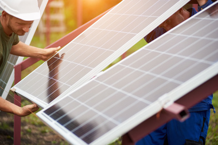 Team of technicians adjusting big shiny solar panel to metal platform on sunny summer warm day. Stand-alone exterior photo voltaic system installation, renewable ecological energy generation concept.の写真素材