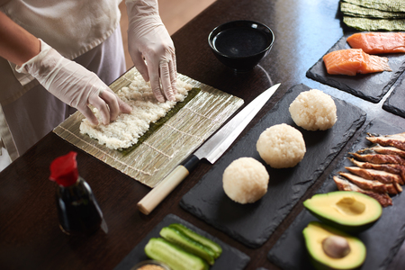 Closeup view of process of preparing rolling sushi. Nori and white rice. Chefs hands touch rice. Chef starts cooking sushiの写真素材