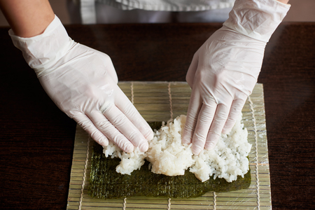 Close-up view of process of preparing rolling sushi. Nori and white rice on bamboo mat. Chefs hands touch rice. Chef starts cooking sushi.の写真素材
