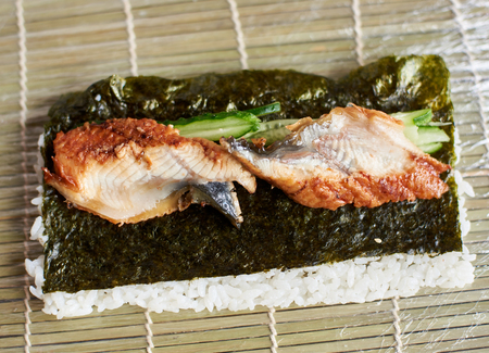 Close-up view of process of preparing rolling sushi. Nori, white rice, cucumber and eel on bamboo mat.の写真素材