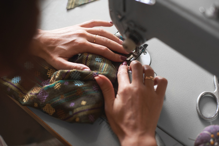 Close-up of female seamstress hands sewing clothing detail on electrical sewing machine. Tailor atelier - handmade exclusive clothes making and repair, private business, creative occupation concept.の写真素材