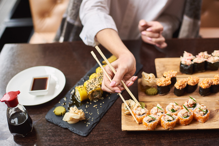 Woman eating and enjoying fresh sushi in luxury restaurant. Female client holding food sticks and eating oriental meal on lunch. Traditional Japanese dish coming with wasabi. Concept of food.の写真素材