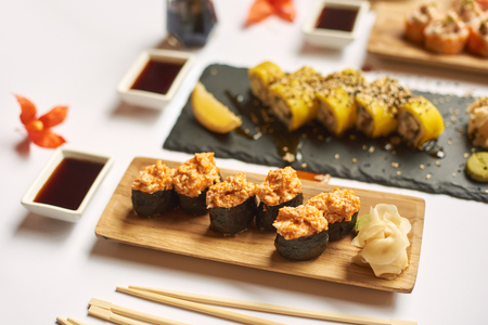 View of sushi roll topped with chopped seafood sticks. Table decorated with physalis, caviar and different vegetables. Delicious Japanese dish served with wasabi and marinated ginger.の写真素材