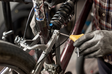 Cropped shot of male mechanic working in bicycle repair shop, repairing mountain bike using special tool, wearing protective glovesの写真素材