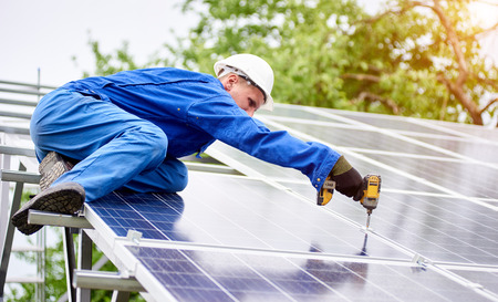 Young construction worker connects photo voltaic panel to solar system using screwdriver on bright sunny day. Alternative cheap sun energy production and profitable financial investment concept.の写真素材