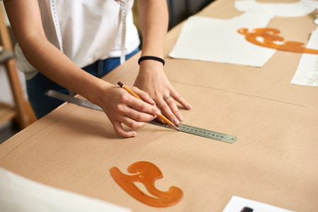 Workplace in design studio. Professional female designer hands close-up making paper patterns using measuring tape, ruler and curves. Exclusive clothes making, creative occupation concept.の写真素材