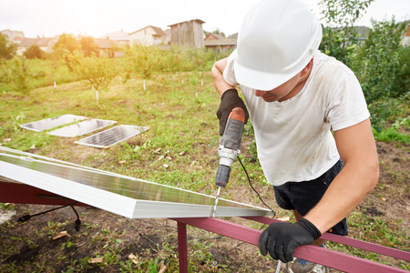 Close-up angled view of technician working with screwdriver connecting solar photo voltaic panel to exterior metal platform. Alternative renewable ecological green sun energy sources concept.の写真素材