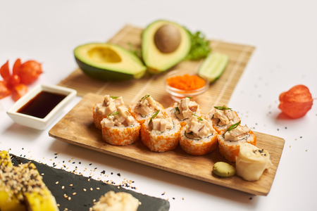 Close up of sushi roll served with soy sauce, wasabi and marinated ginger. Tasty meal ready and waiting for clients during lunch. Still life decorated with physalis, avocado, cucumber and caviar.の写真素材