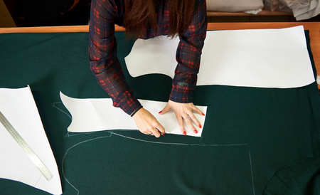 Close-up of woman hands making chalk markings of paper patterns on green fabric copy space surface before cutting details for future jacket or costume. Fashionable garment tailoring at the studio.の写真素材