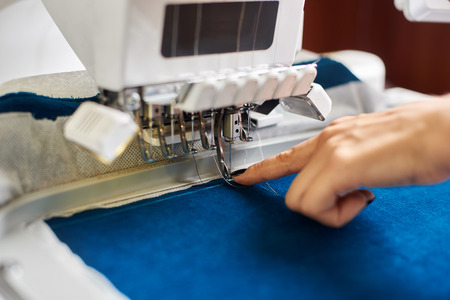 Close-up of woman hand at computerized embroidery machine on background of bright blue textile detail. Specially engineered machine with multi-needle fixed embroidery head.の写真素材