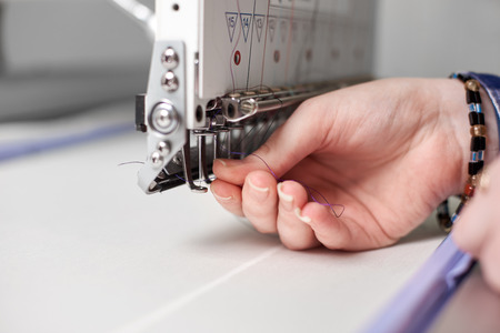 Close-up of female hands filling thread in modern embroidery machine on bright blurred white copy space background. Industrial embroidery, commercial production and high quality results concept.の写真素材