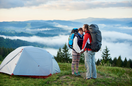 Romantic couple of lovers resting in the mountains in the morning on the background of mountains with haze and sky with clouds near camping. Concept of active outdoor lifestyleの写真素材