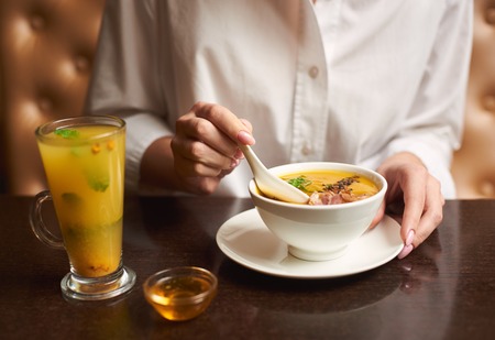 Crop of woman in white blouse holding in hands white bowl with orange cream soup. Female posing in...