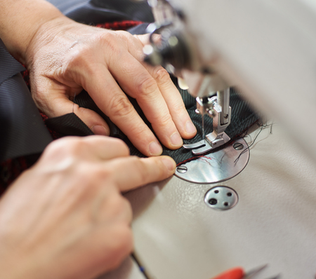 Top view of woman hands stitching garment on professional sewing machine at workplace. Tailor hands...