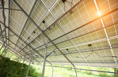 Interior of stand-alone photo voltaic solar system secured on metal rear legs on green grass, lit by summer sun. Alternative energy, environment protection and cheap electricity production concept.の写真素材