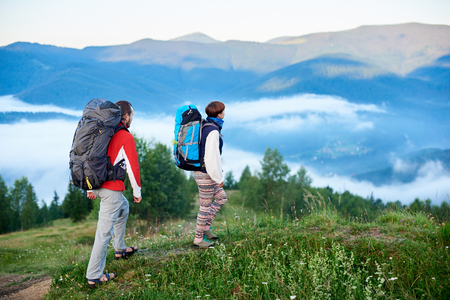 Two tourists with backpacks in a hike on the mountains of the Carpathians on a blurred background of mountains with a fog on them. Concept of active outdoor trekking lifestyleの写真素材