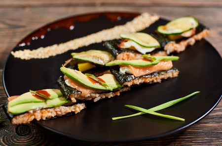 Close up view delicious sushi with nori rice and avocado on black plate served on the wooden tableの写真素材