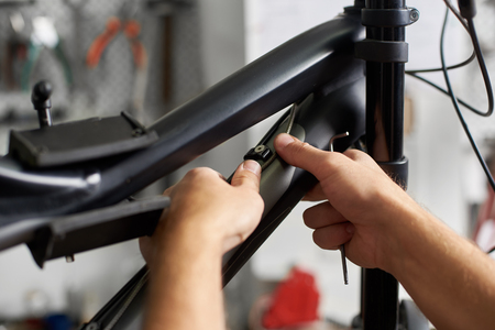 Cropped shot of serviceman working in bicycle repair shop, bicyclist fixing bike using special toolの写真素材